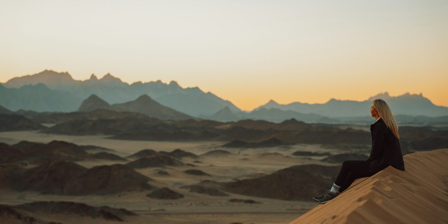 a woman sitting on top of a sand dune